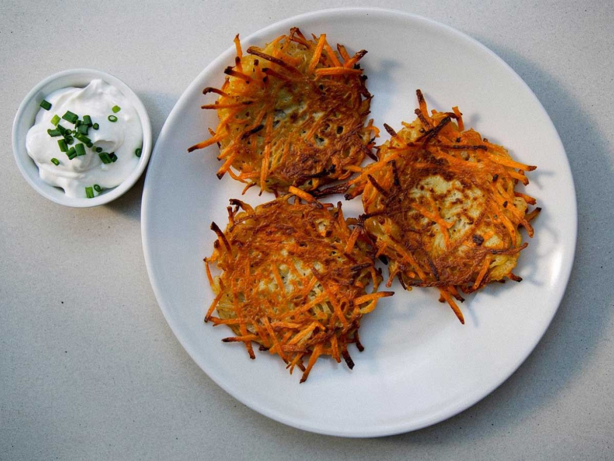 3 aardappel-wortel pannenkoekjes op een bord, met daarnaast de kruidendip.