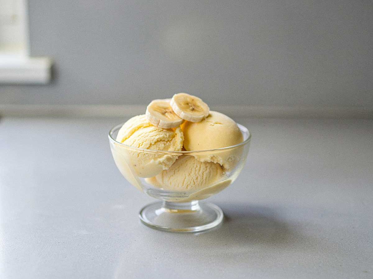 4 bollen zelfgemaakt banaan roomijs in een glazen dessertschaaltje, met 2 plakjes banaan erop.