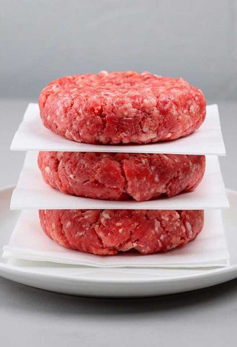 3 nog niet gebakken beefburgers op een wit bordje met vetvrij papier ertussen.