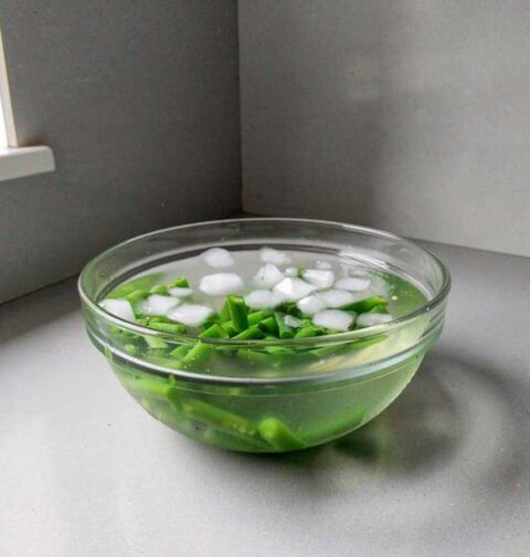 Een glazen schaal met ijswater om het koken van deze geblancheerde sperziebonen te stoppen.
