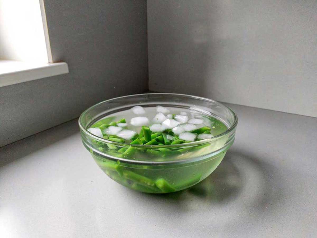 Een glazen schaal met ijswater om het koken van deze geblancheerde sperziebonen te stoppen.