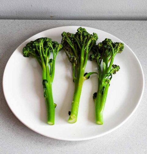 Drie stelen gekookte broccolini op een wit bord.