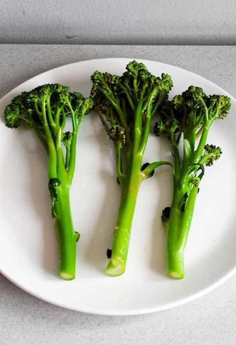 Drie stelen gekookte broccolini op een wit bord.