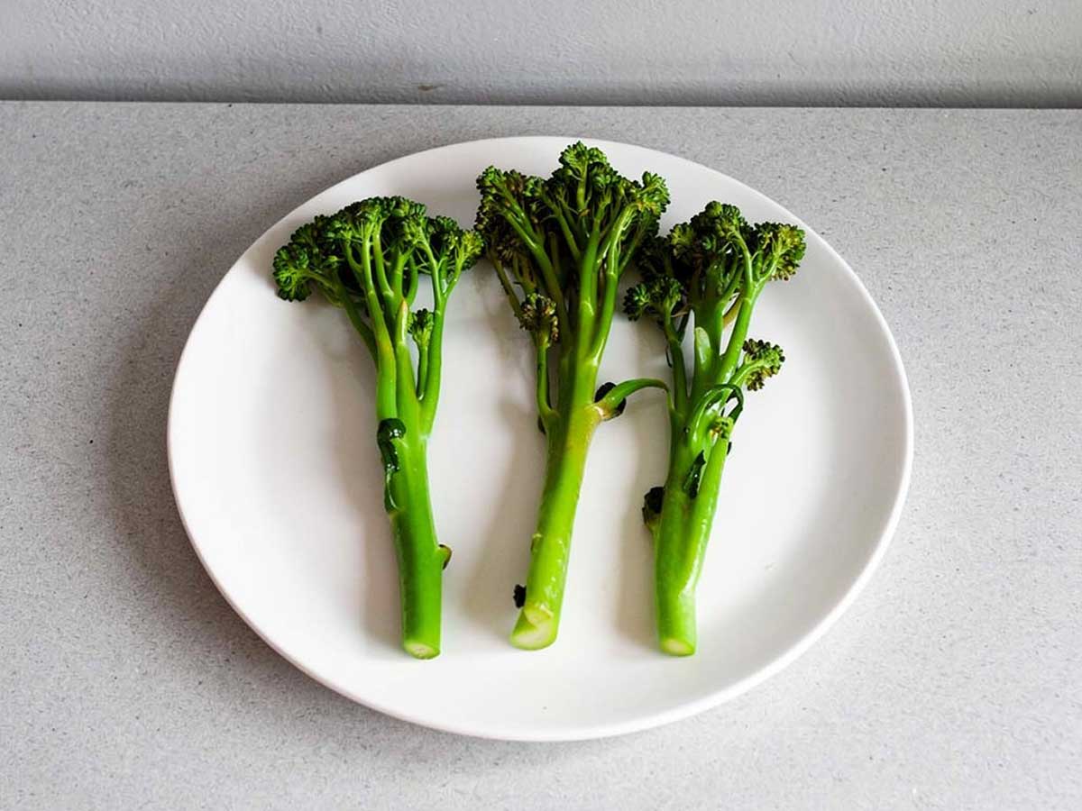 Drie stelen gekookte broccolini op een wit bord.