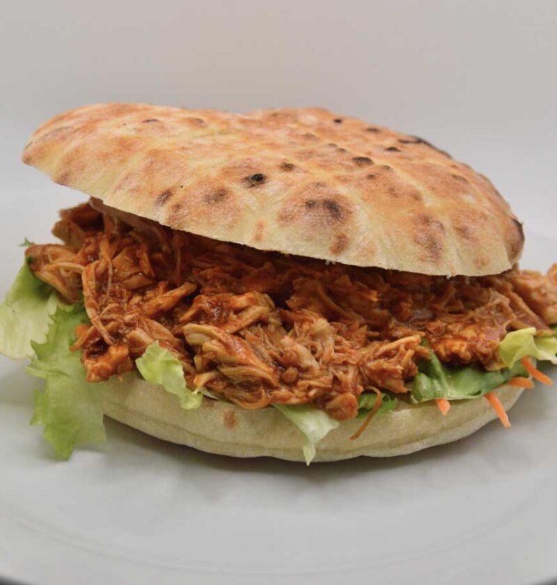 Een broodje pulled pork op een wit bord.