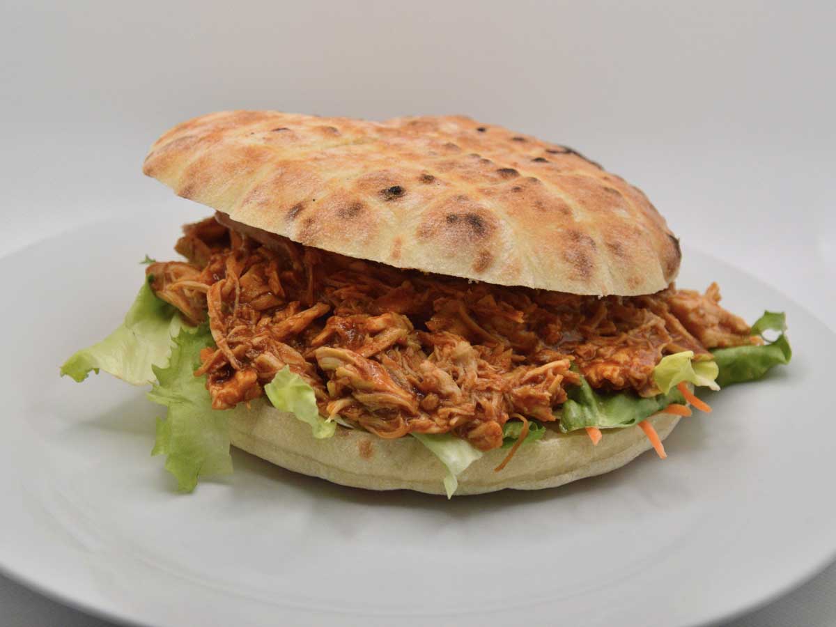 Een broodje pulled pork op een wit bord.