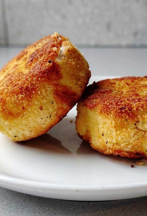2 gepaneerde en gebakken camembert op een wit bord.