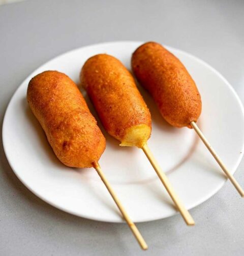 3 gefrituurde corndogs op een wit bord.