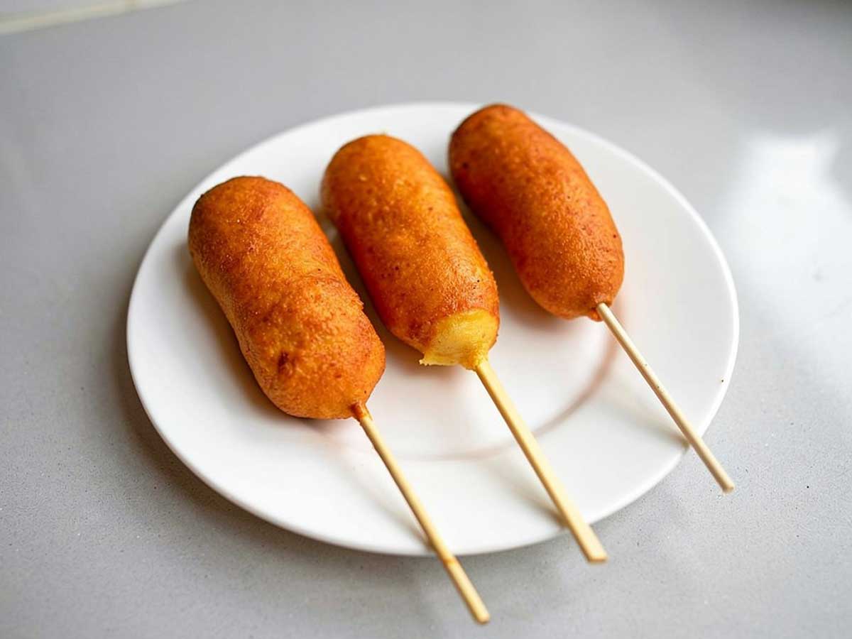 3 gefrituurde corndogs op een wit bord.
