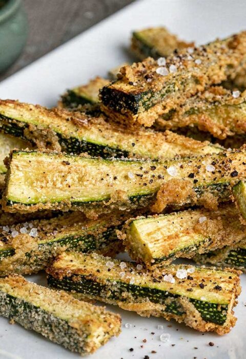 Een rechthoekige witte schaal met daarop in de oven gemaakte courgette frieten.