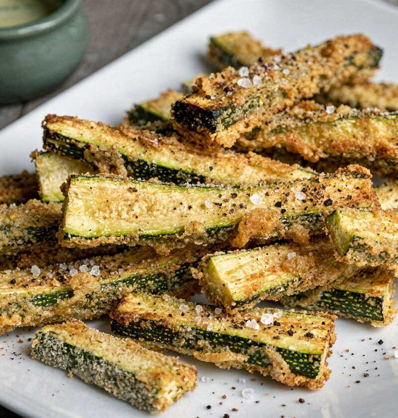 Een rechthoekige witte schaal met daarop in de oven gemaakte courgette frieten.