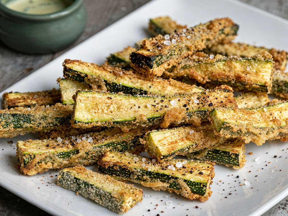 Een rechthoekige witte schaal met daarop in de oven gemaakte courgette frieten.