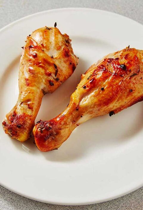 2 heerlijk gebakken drumsticks op een wit bord.