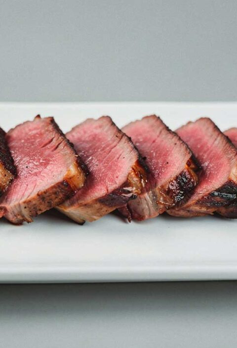 Een in plakjes gesneden entrecote, op een witte schaal.