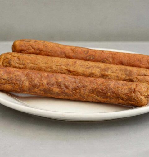 3 perfect gefrituurde frikandellen liggen op een wit bord.