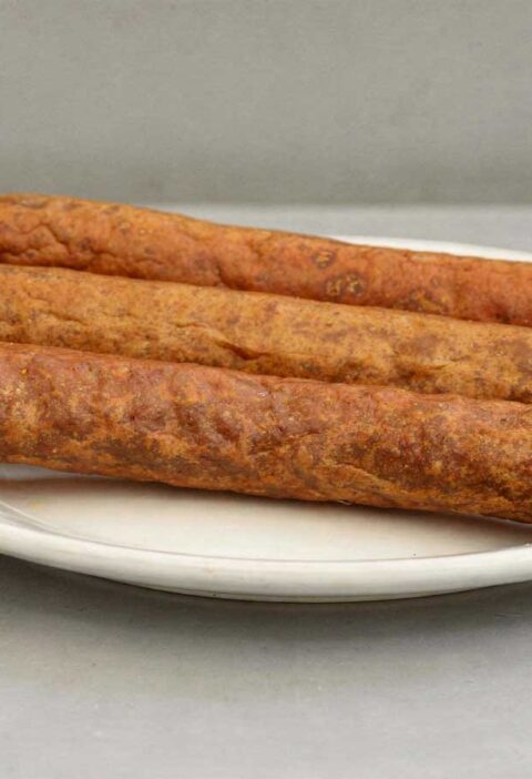 3 perfect gefrituurde frikandellen liggen op een wit bord.