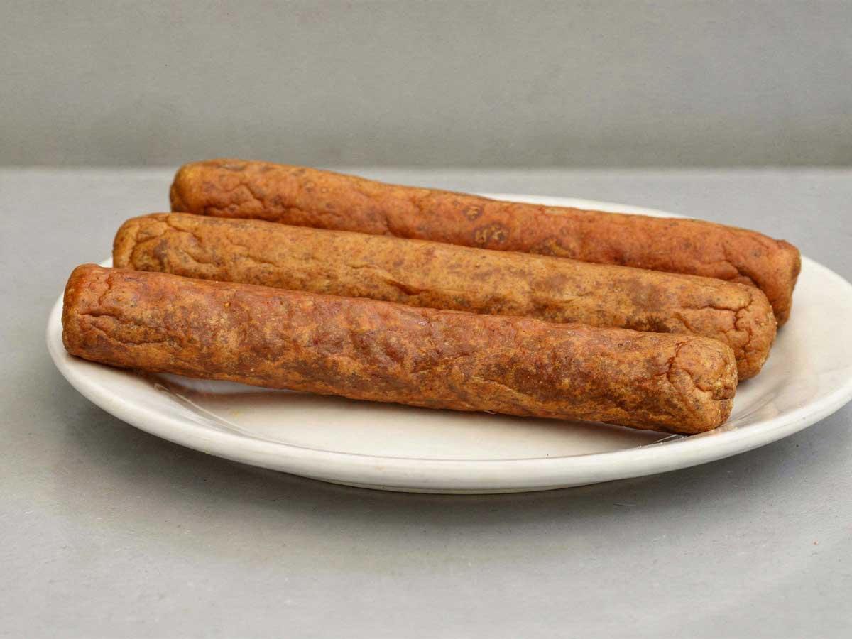 3 perfect gefrituurde frikandellen liggen op een wit bord.