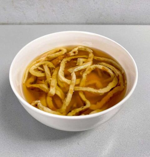 Een witte soepkom met fritattensoep, een soort pannenkoekensoep.