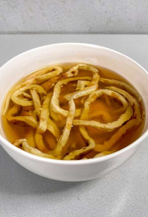 Een witte soepkom met fritattensoep, een soort pannenkoekensoep.