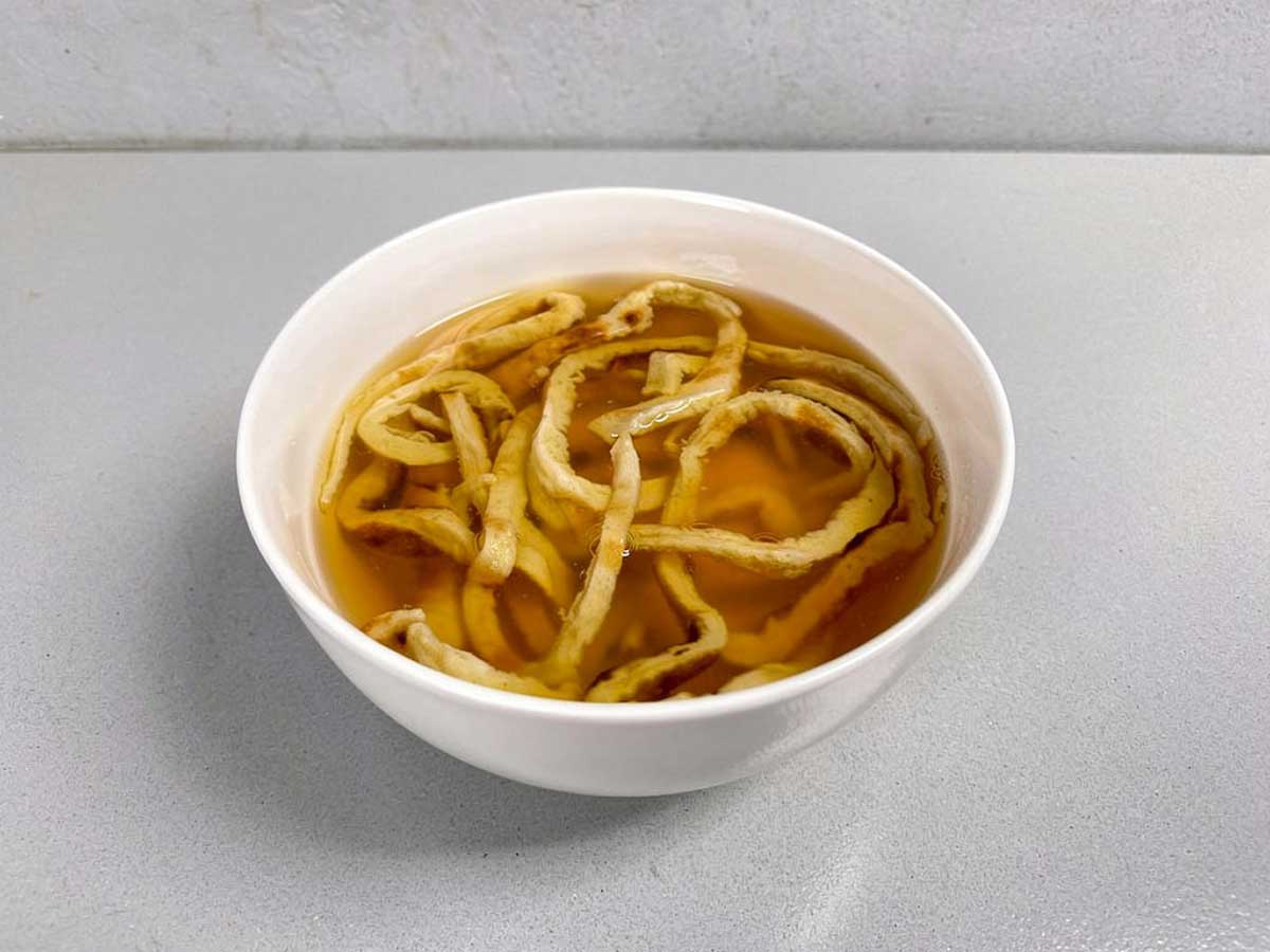 Een witte soepkom met fritattensoep, een soort pannenkoekensoep.