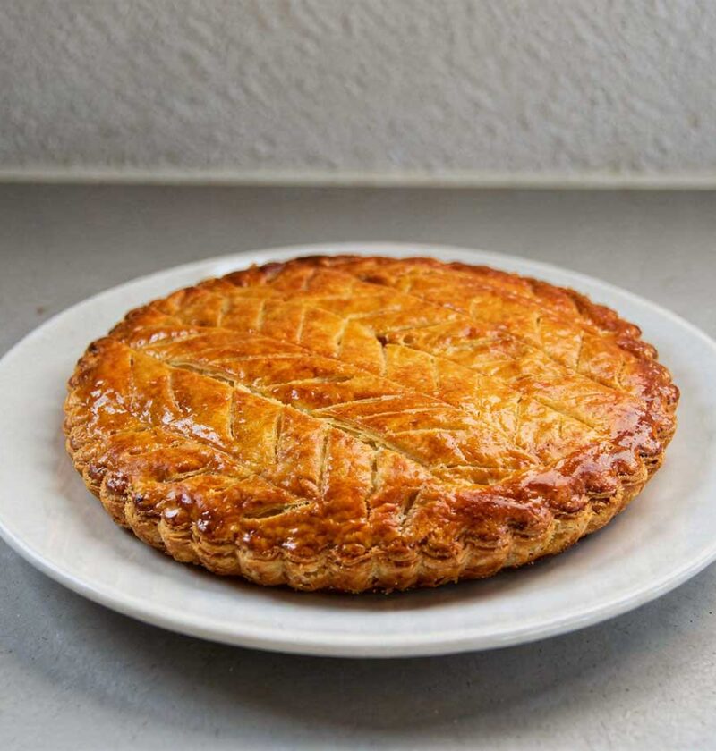 Een hele galette des rois op een wit rond bord.