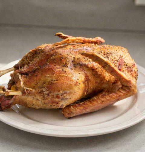 Een hele gebraden gans op een groot wit bord.