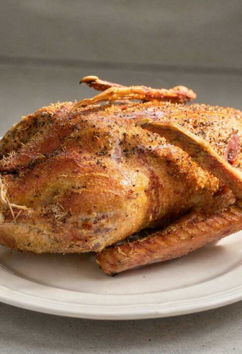 Een hele gebraden gans op een groot wit bord.