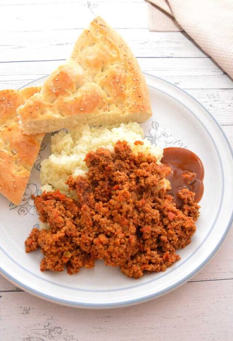 Een bord met rul gebakken gehakt, rijst, Turks brood en saus.