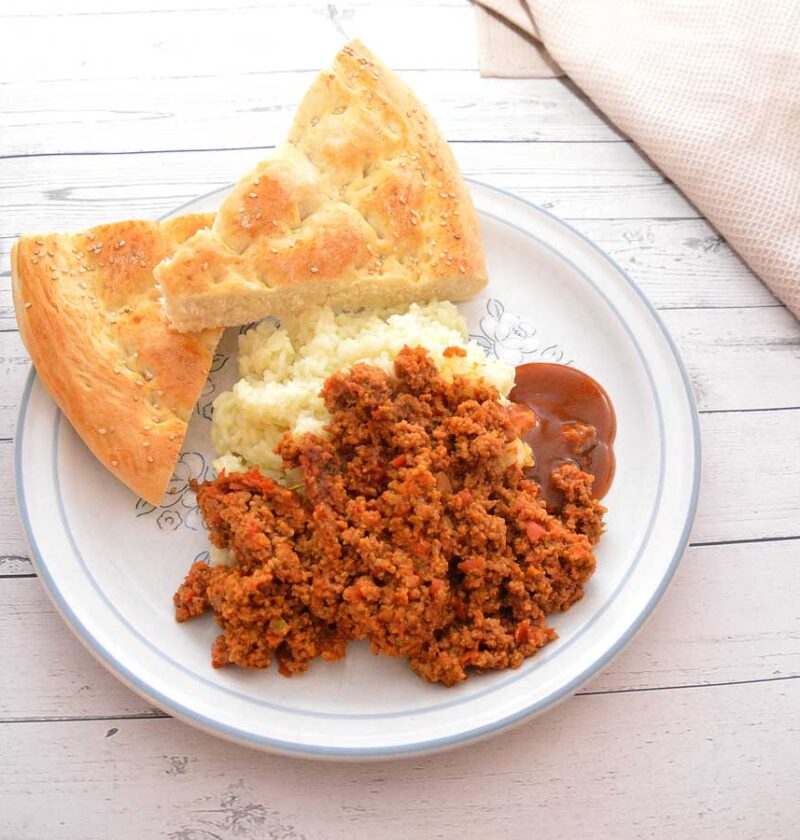 Een bord met rul gebakken gehakt, rijst, Turks brood en saus.