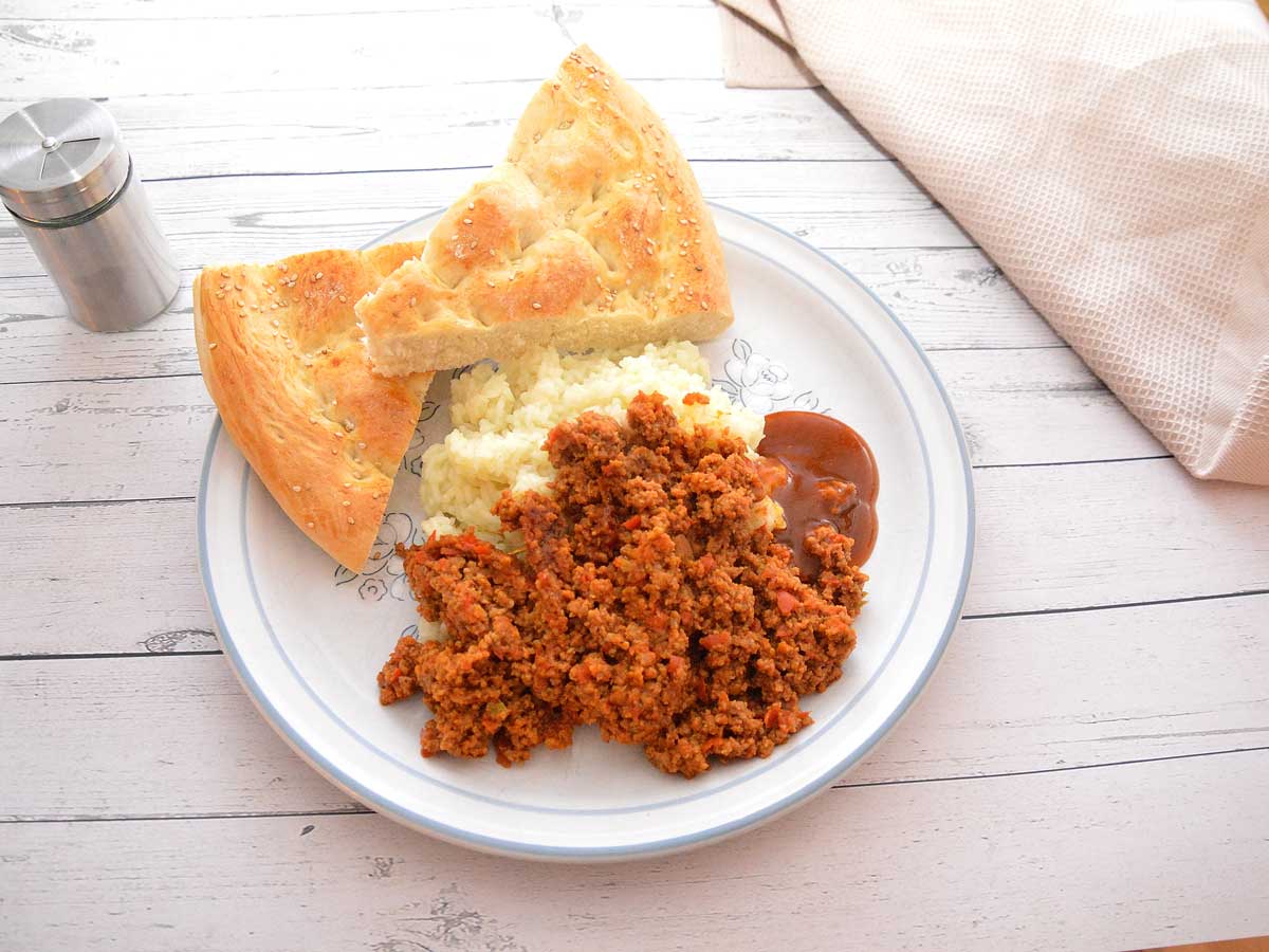 Een bord met rul gebakken gehakt, rijst, Turks brood en saus.