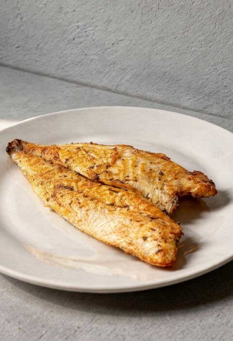 Een gebakken goudbrasemfilet, oftewel doradefilet, op een wit bordje.