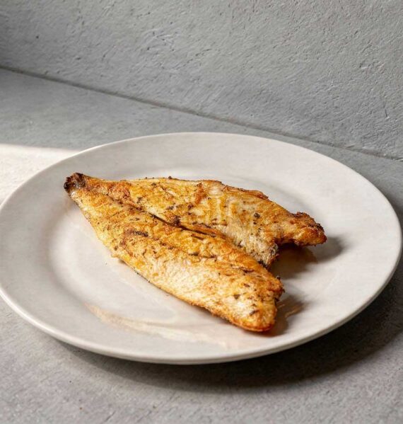 Een gebakken goudbrasemfilet, oftewel doradefilet, op een wit bordje.