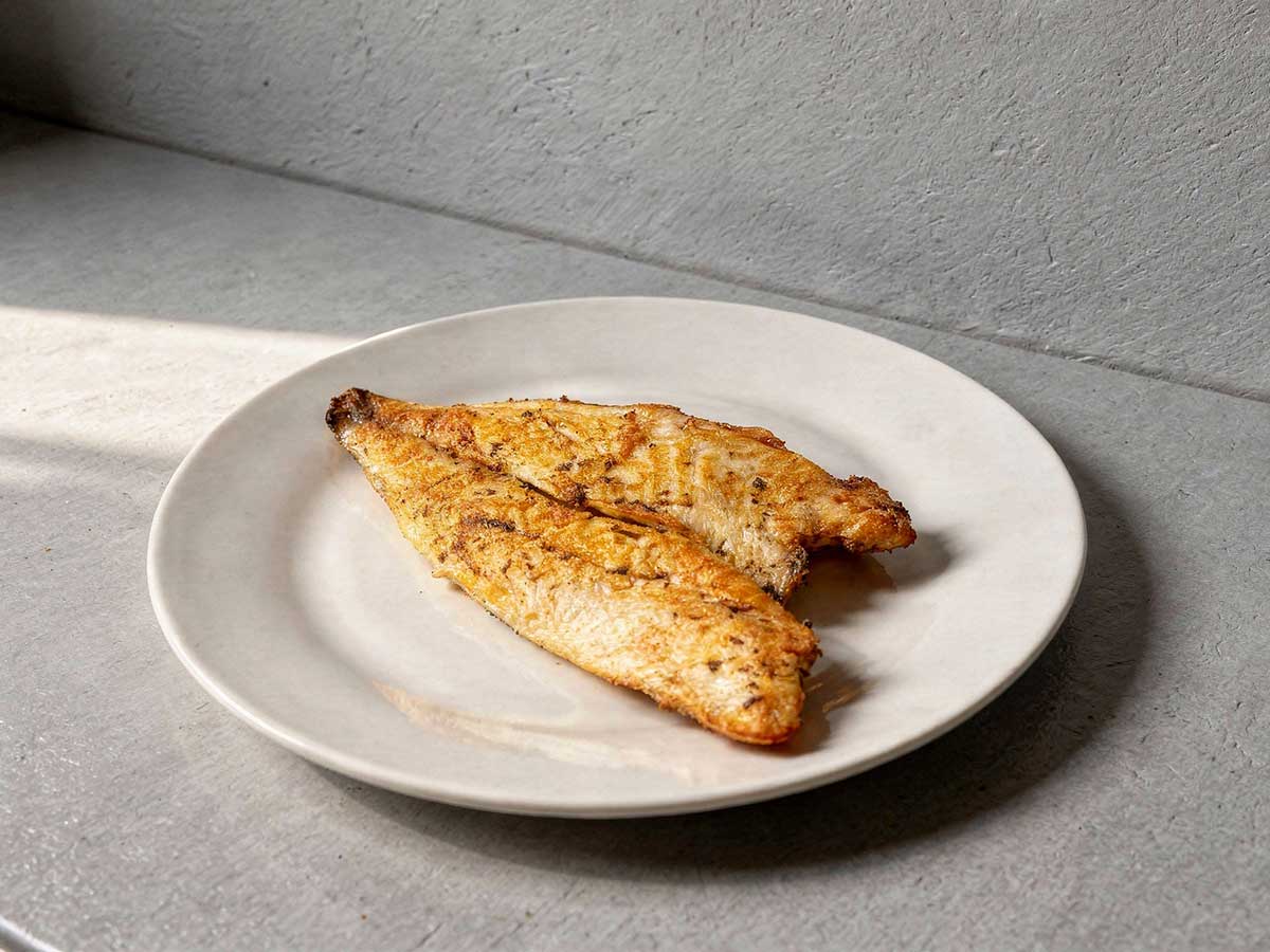 Een gebakken goudbrasemfilet, oftewel doradefilet, op een wit bordje.