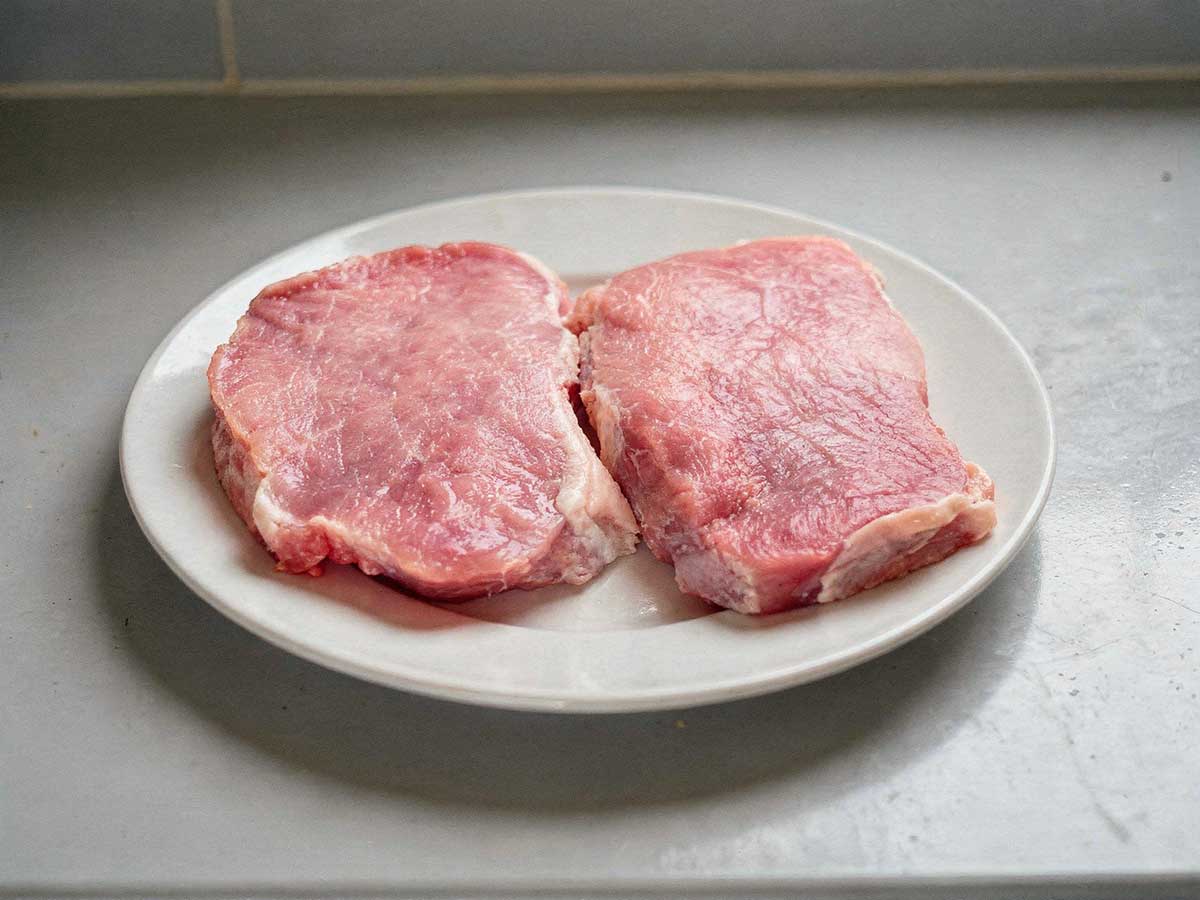 2 ongebakken hamlappen liggen op een wit bord.