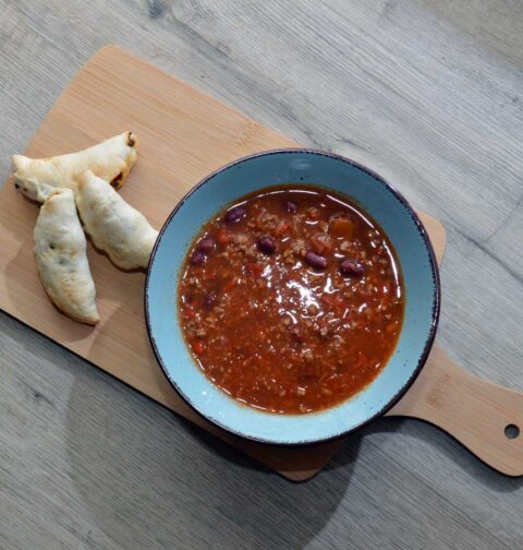 Een kom met opgewarmde chili concarne en wat kleine broodjes.