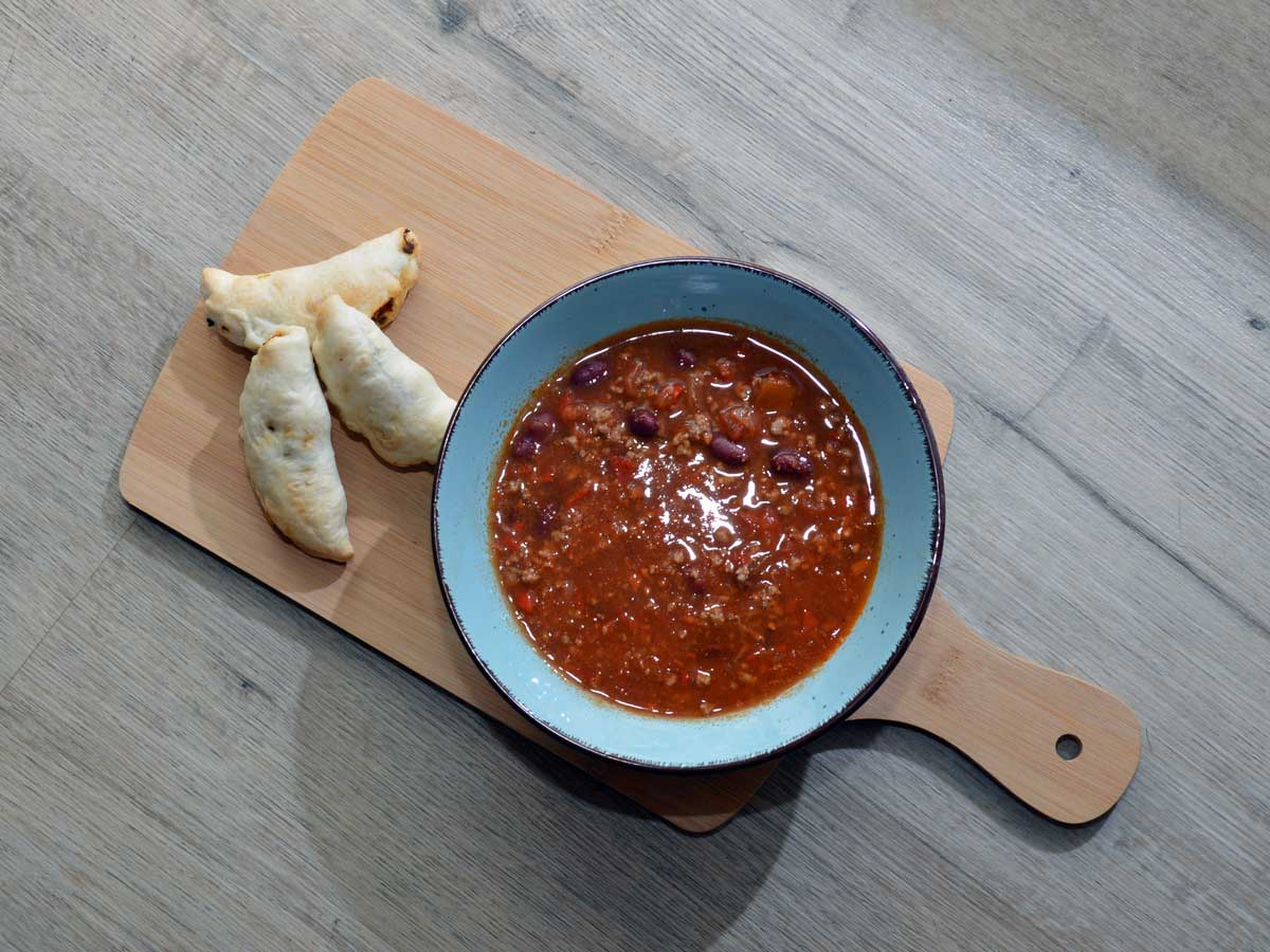 Een kom met opgewarmde chili concarne en wat kleine broodjes.