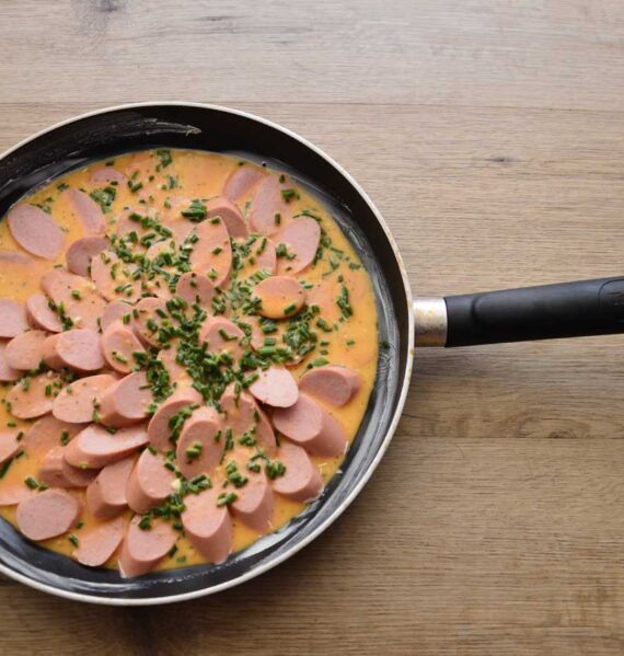 In plakjes gesneden knakworst die emt een saus is opgewarmd in een koekenpan.