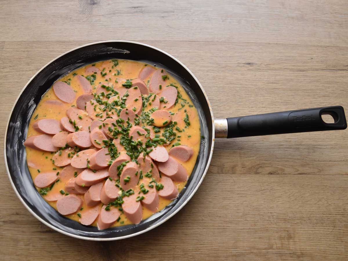 In plakjes gesneden knakworst die emt een saus is opgewarmd in een koekenpan.