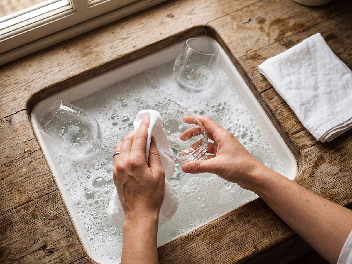 Twee handen boven een spoelbakwaarin glazen worden af gewassen.
