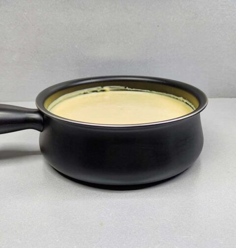 Een zwarte fonduepan met daarin kasfonue die opgewarmd moet worden.