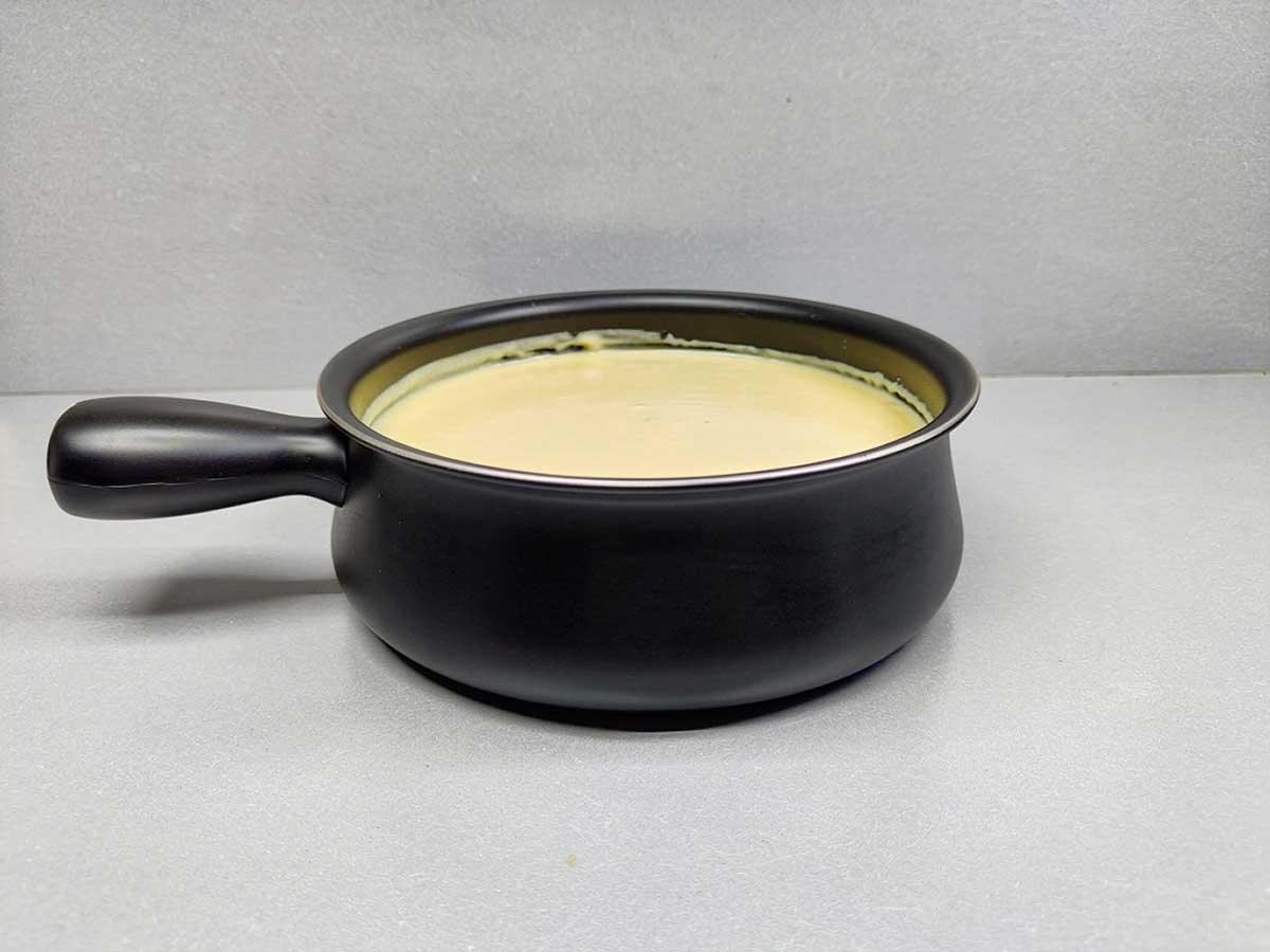 Een zwarte fonduepan met daarin kasfonue die opgewarmd moet worden.