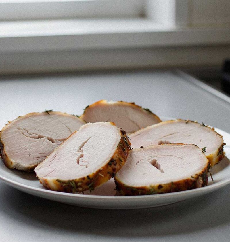 Een in plakken gesneden gebraden kalkoenrollade op een wit bord.