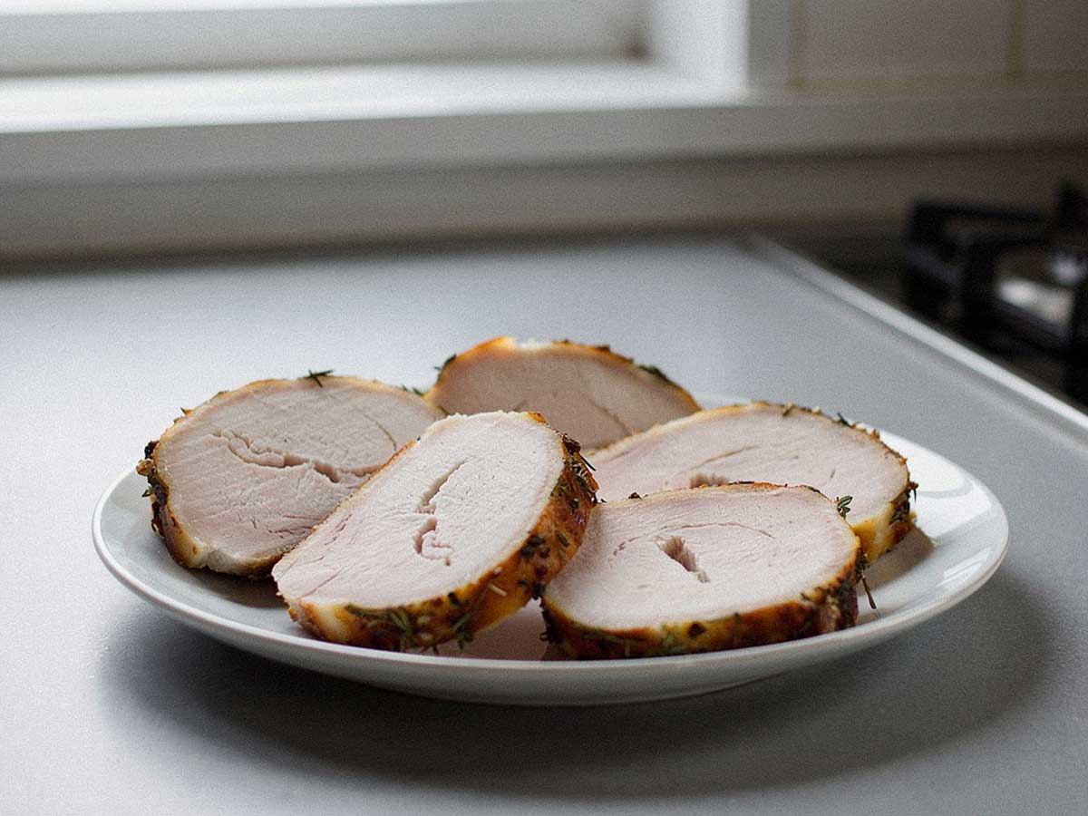 Een in plakken gesneden gebraden kalkoenrollade op een wit bord.