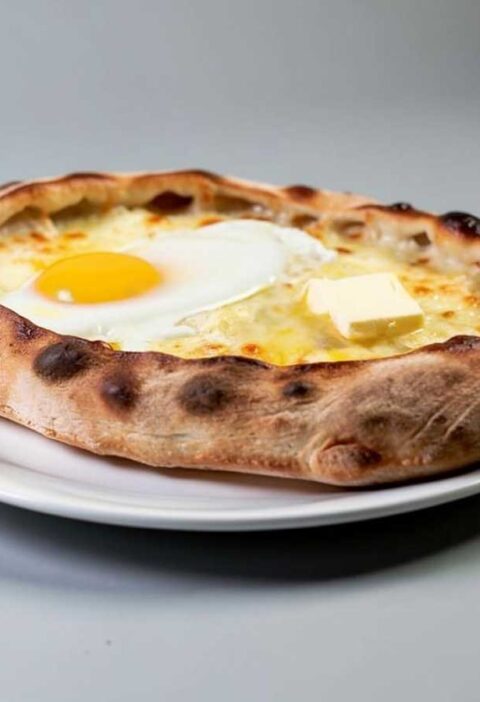 Een hele khachapuri op een wit bord.