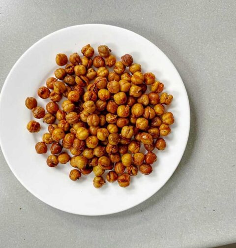 Een wit bord met daarom een portie geroosterde kikkererwten.