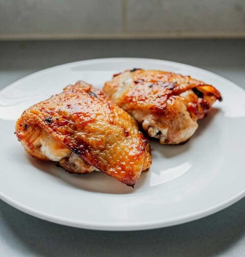 2 gebakken kipdijen op een wit bord.