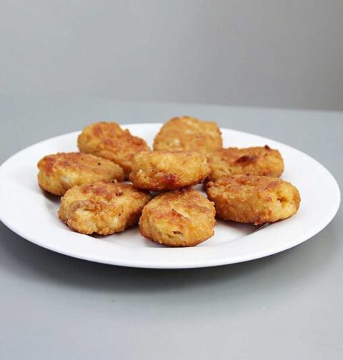 8 gefrituurde kipnuggets op een wit bordje.