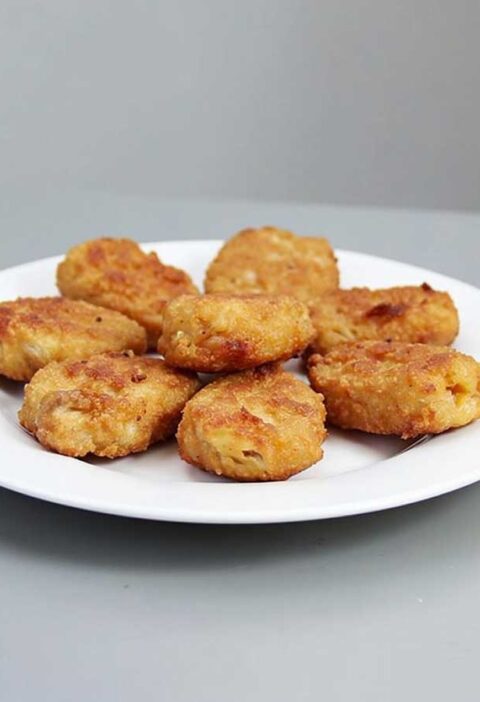 8 gefrituurde kipnuggets op een wit bordje.