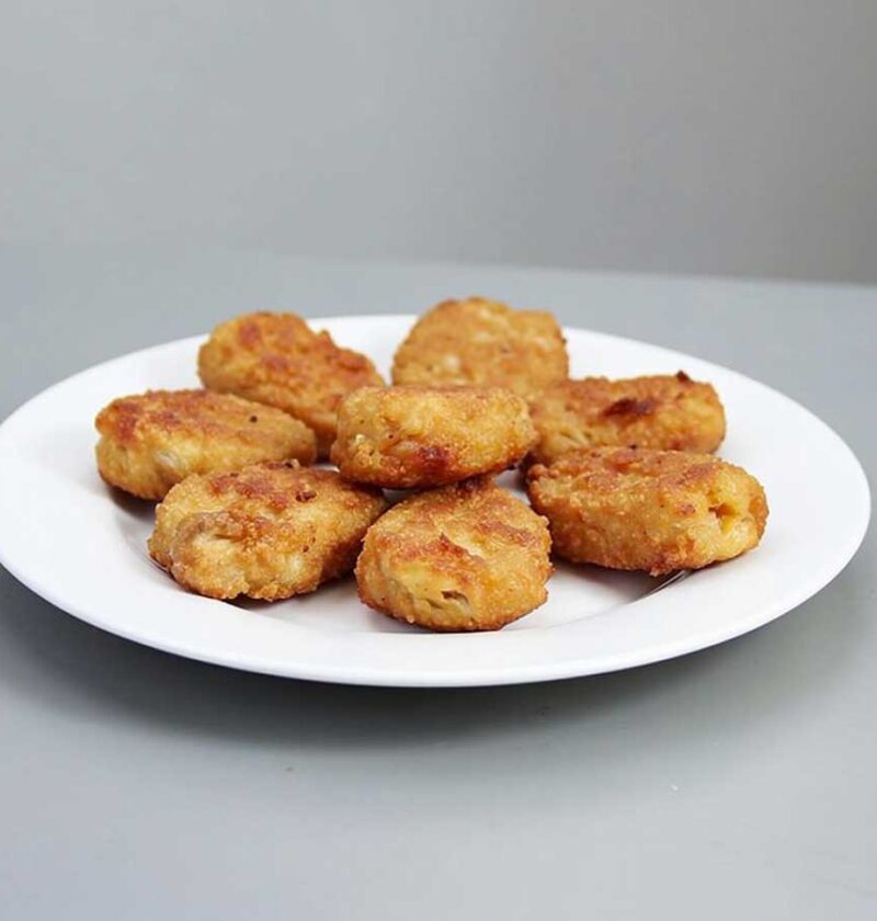8 gefrituurde kipnuggets op een wit bordje.