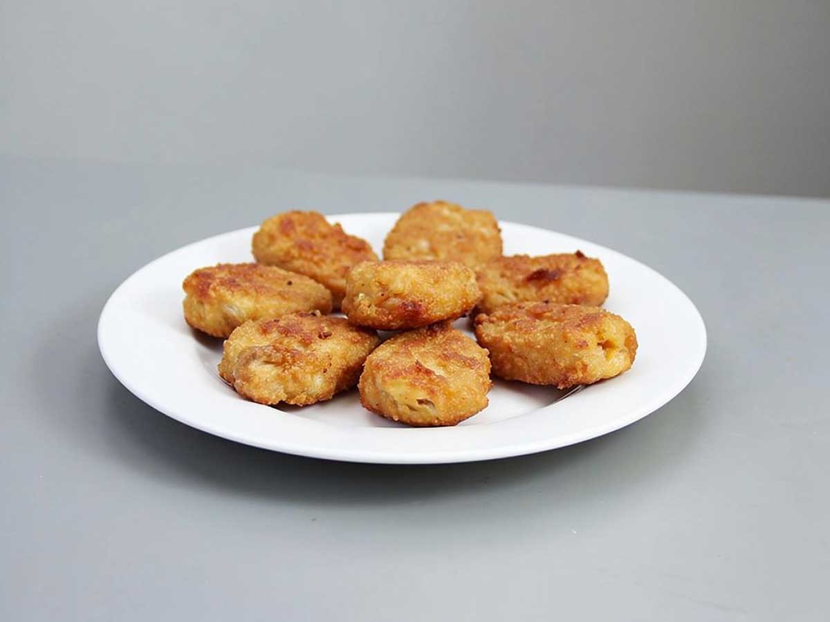 8 gefrituurde kipnuggets op een wit bordje.